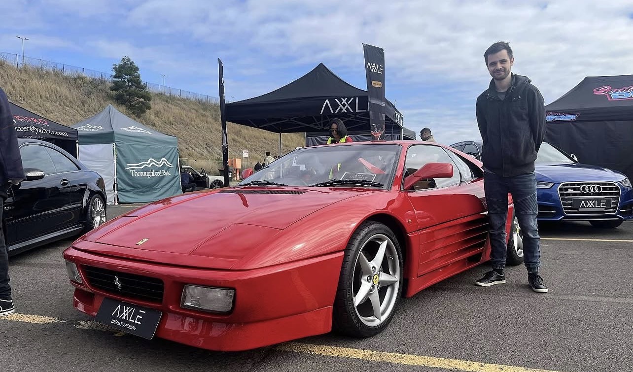 James, owner of Detail Xpress Mobile Detailing, standing beside a red Ferrari at a car show