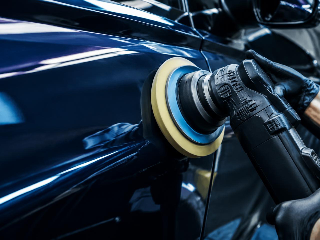 Machine polishing a dark blue car panel to a glossy finish during an exterior detail